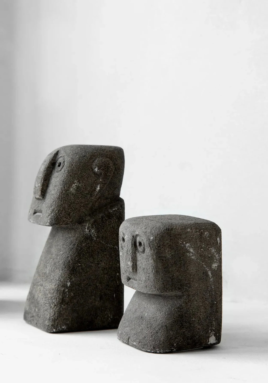 Sculptures décoratives en pierre grise avec visages stylisés sur bases effilées