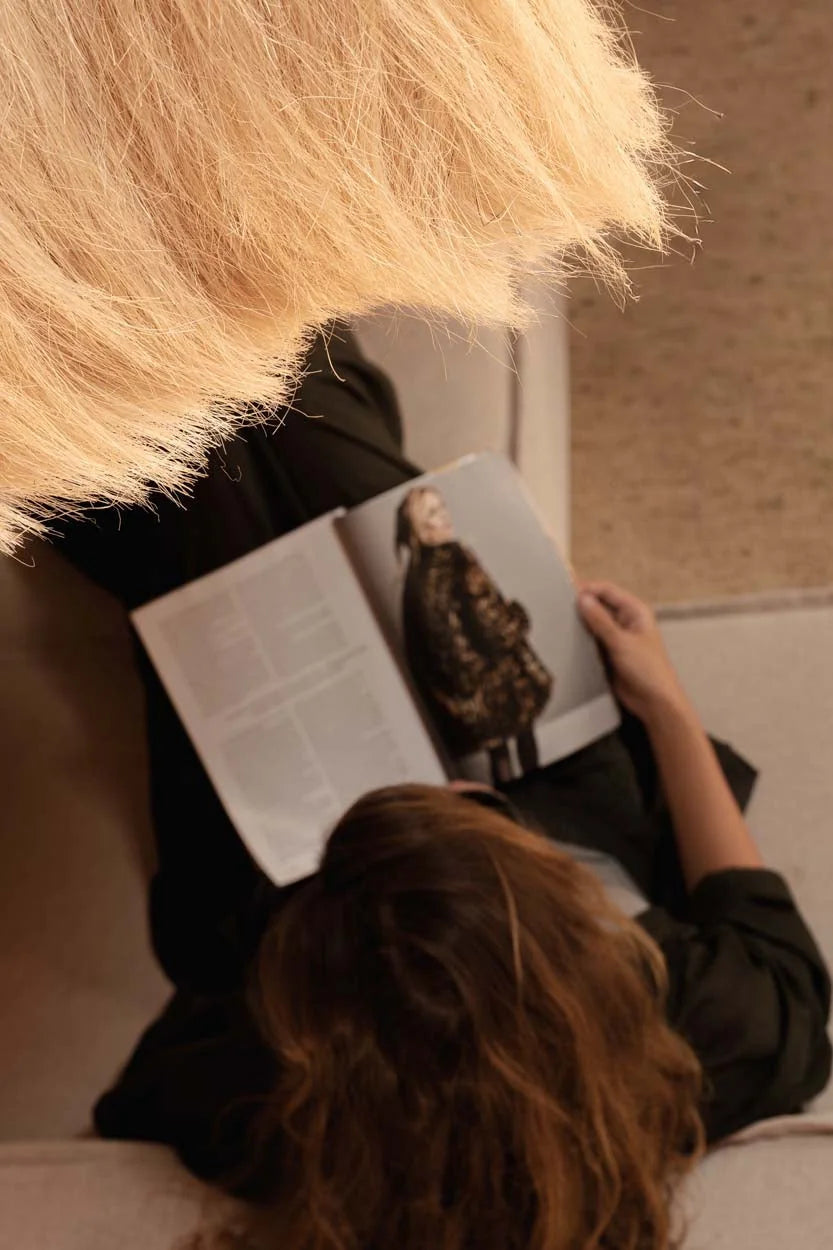 Personne blonde lit magazine avec manteau sombre sous suspension cloche paille frangée Ø60 cm