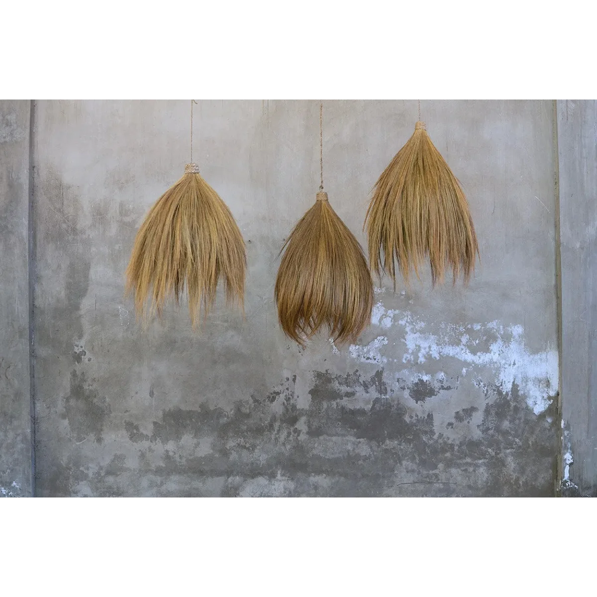 Suspensions coniques en fibre naturelle beige suspendues contre un mur en béton