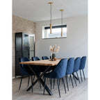 Salle à manger avec table en bois et chaises bleues, éclairage suspension cylindrique en laiton