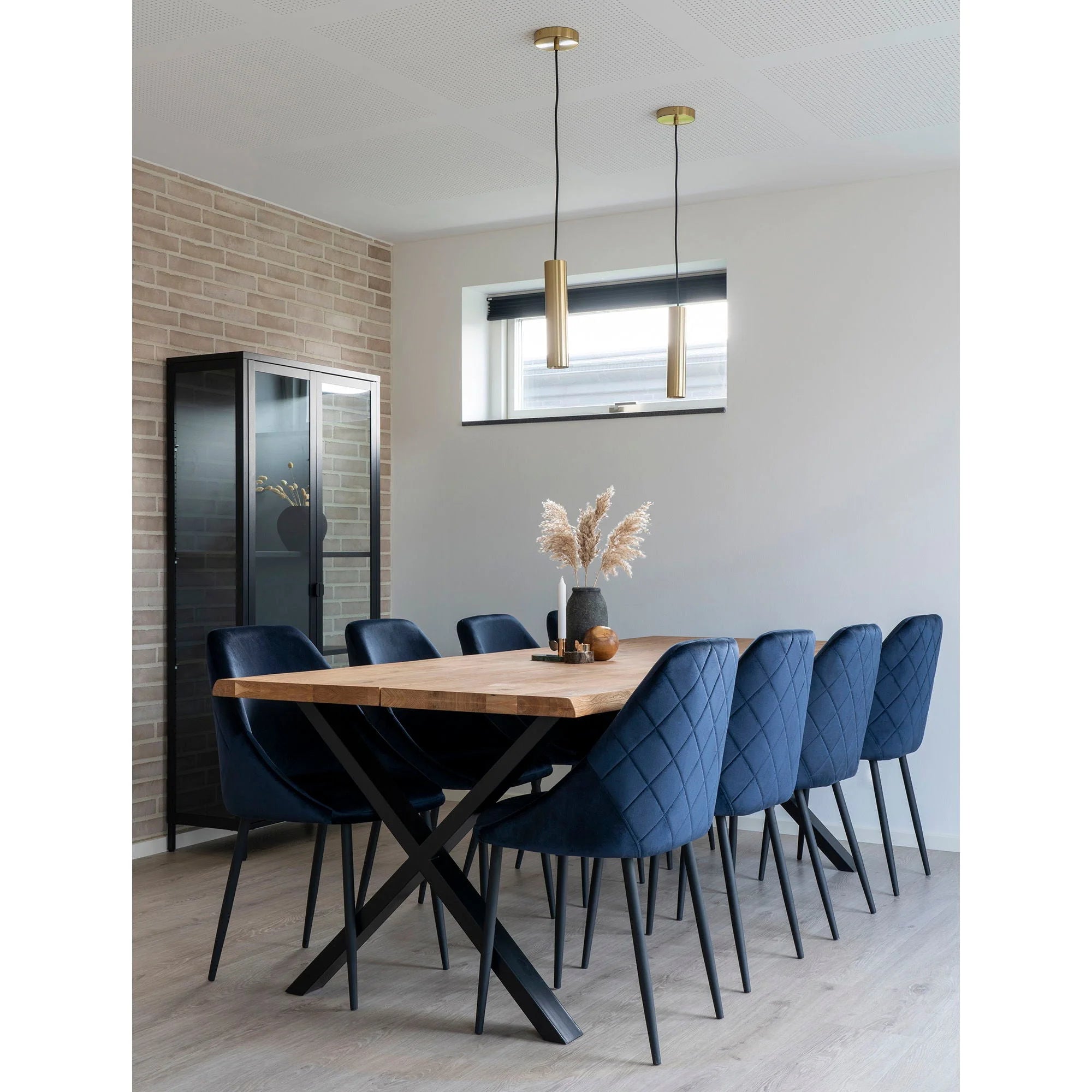 Salle à manger avec table en bois et chaises bleues, éclairage suspension cylindrique en laiton