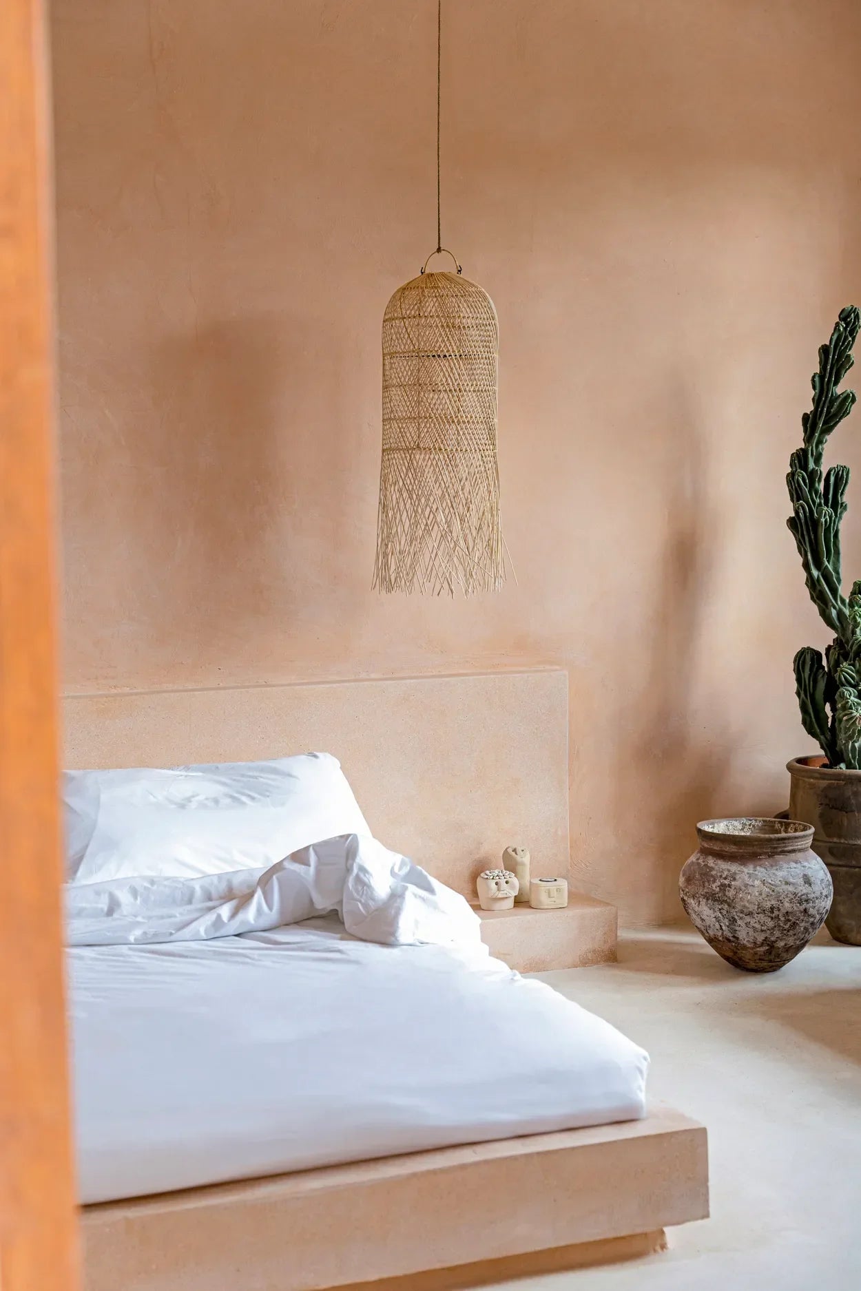 Chambre minimaliste avec suspension cylindrique en rotin naturel et franges