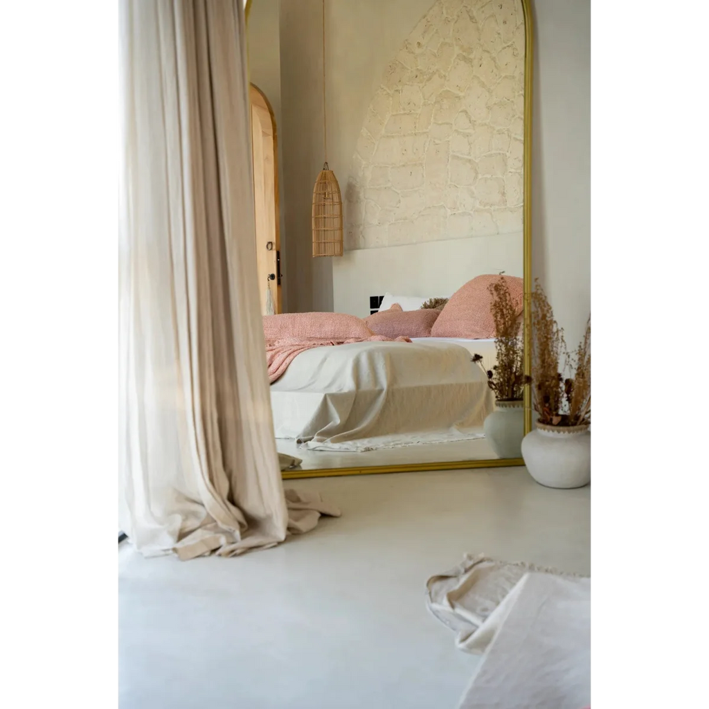 Miroir pleine longueur avec cadre en or refletant un lit avec literie rose