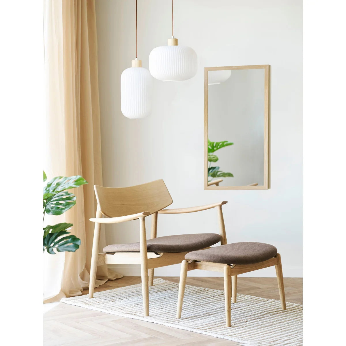 Fauteuil en bois clair avec coussin foncé et ottoman assorti, Suspension globe en verre opalin blanc Ø30 cm