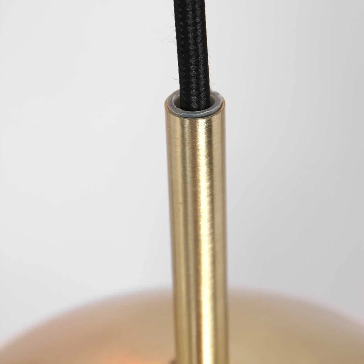 Détail d’un composant de luminaire cylindrique en or avec câble électrique noir tressé
