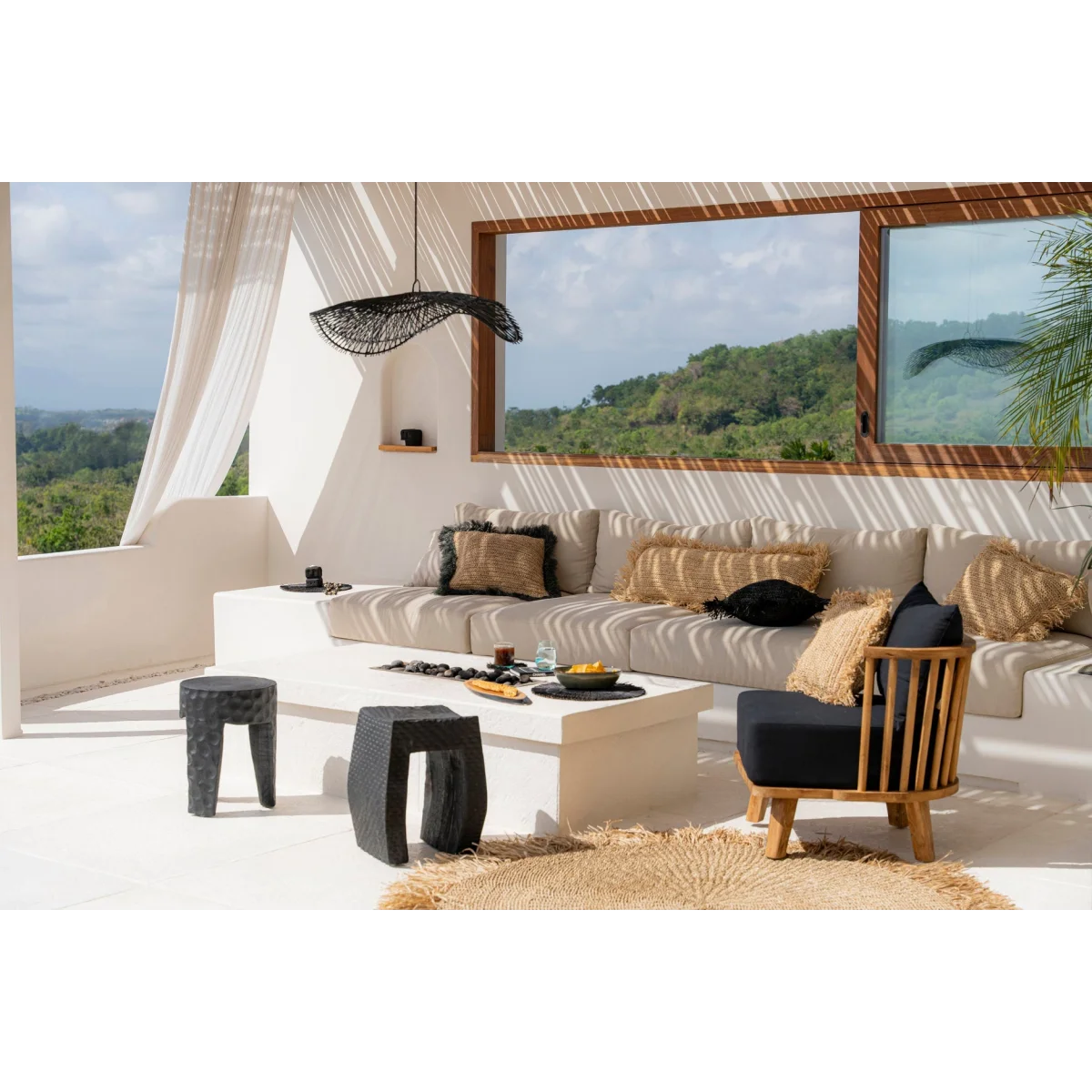 Coin salon extérieur avec canapé modulable clair, fauteuil foncé, table blanche et tabourets