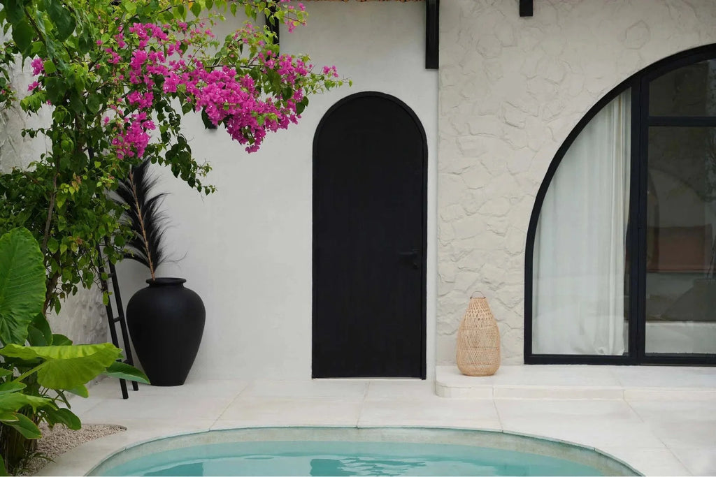 Porte arquée noire dans un mur blanc à côté d’une piscine, décoration naturelle en rotin