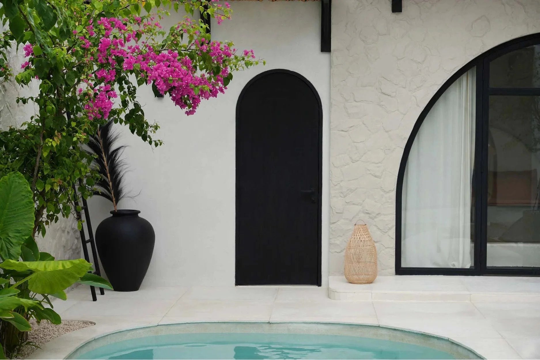 Porte arquée noire dans un mur blanc à côté d’une piscine, décoration naturelle en rotin