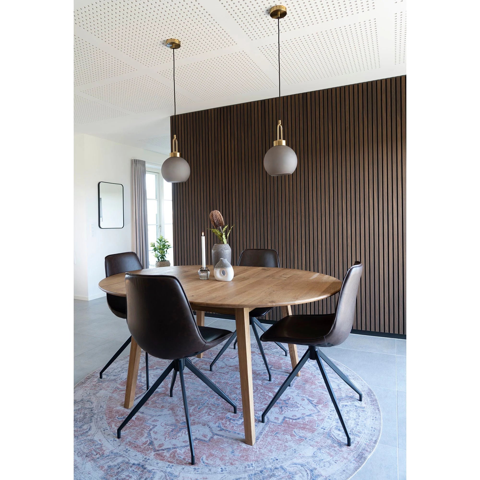 Suspension sphérique en verre fumé mat et laiton doré au-dessus d’une salle à manger avec table ronde
