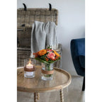 Vase en verre transparent avec bande en osier, bouquet de fleurs colorées, table ronde en bois de manguier