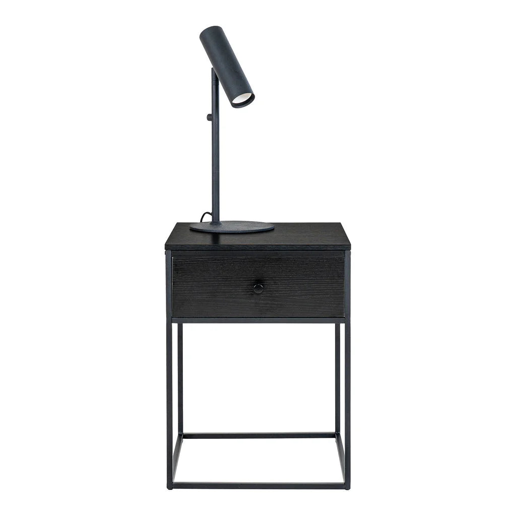Table de chevet noire en acier et MDF avec tiroir et lampadaire éclairant la pièce