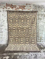 Tapis rectangulaire laine géométrique beige noir 310x204 cm sur mur brique