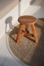 Tabouret en bois à trois pieds sur le tapis rond en jonc de mer et coton naturel