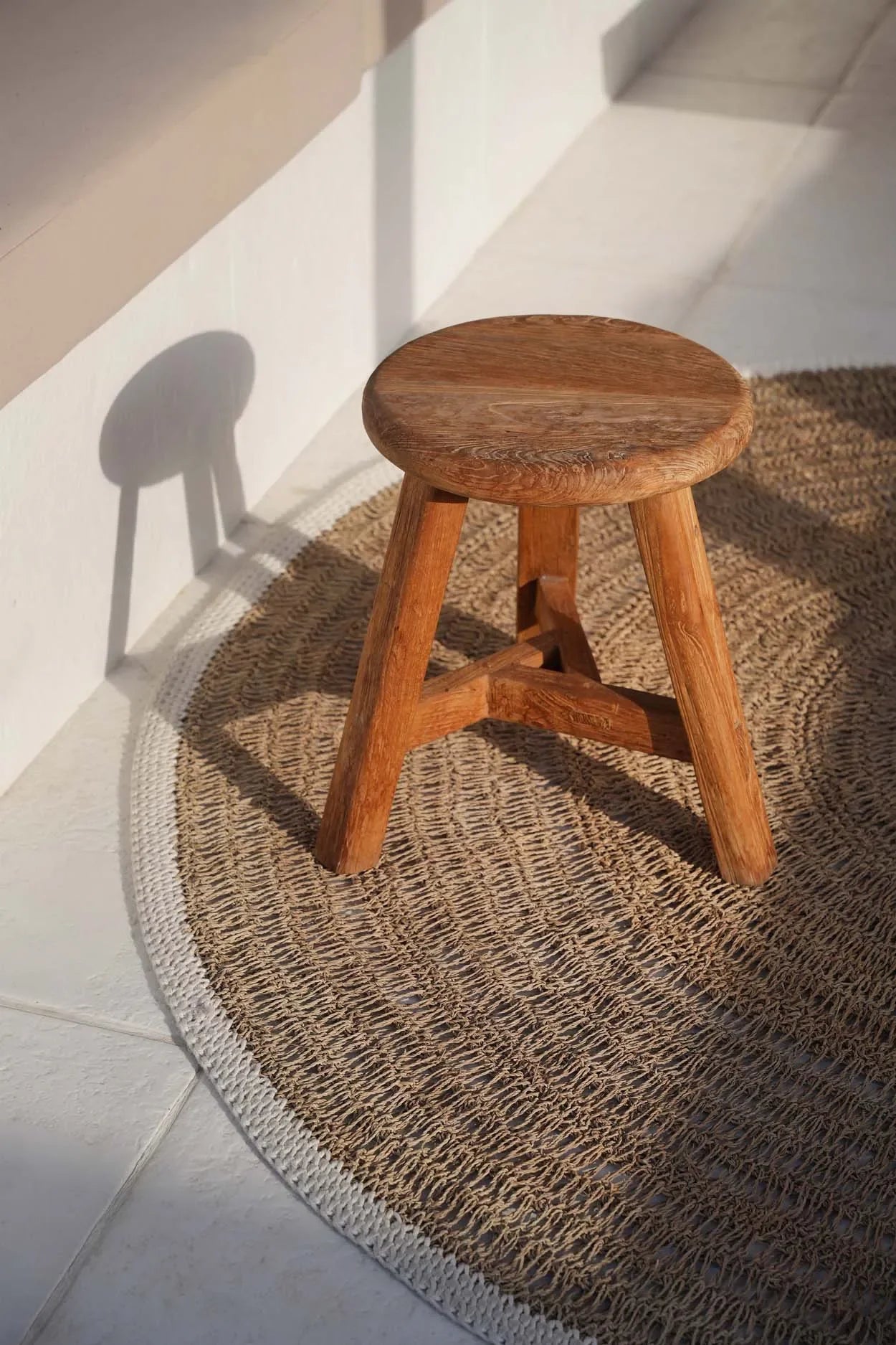 Tabouret en bois à trois pieds sur le tapis rond en jonc de mer et coton naturel