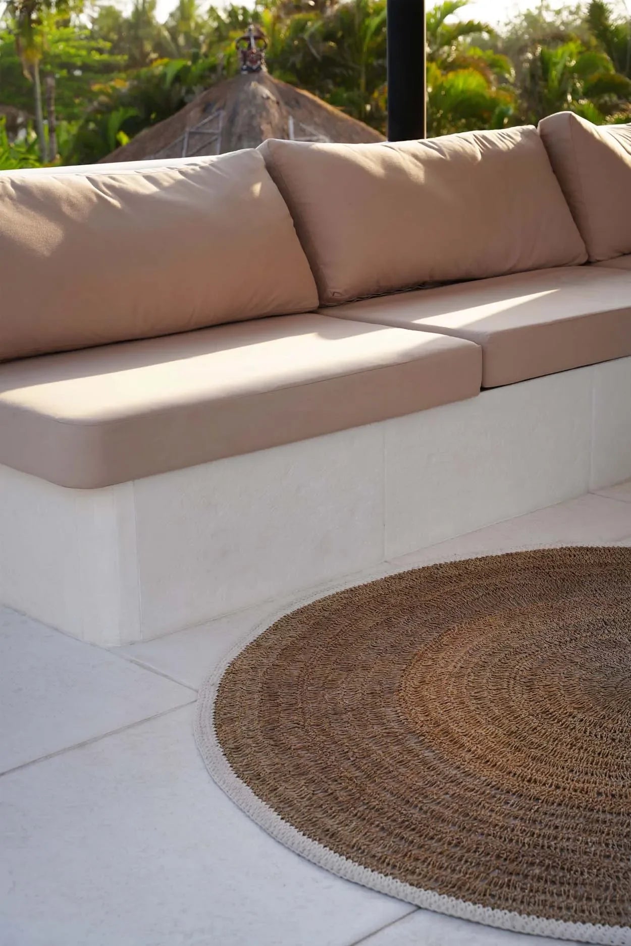 Canapé d’extérieur aux tons neutres avec tapis rond en jonc de mer et coton blanc naturel
