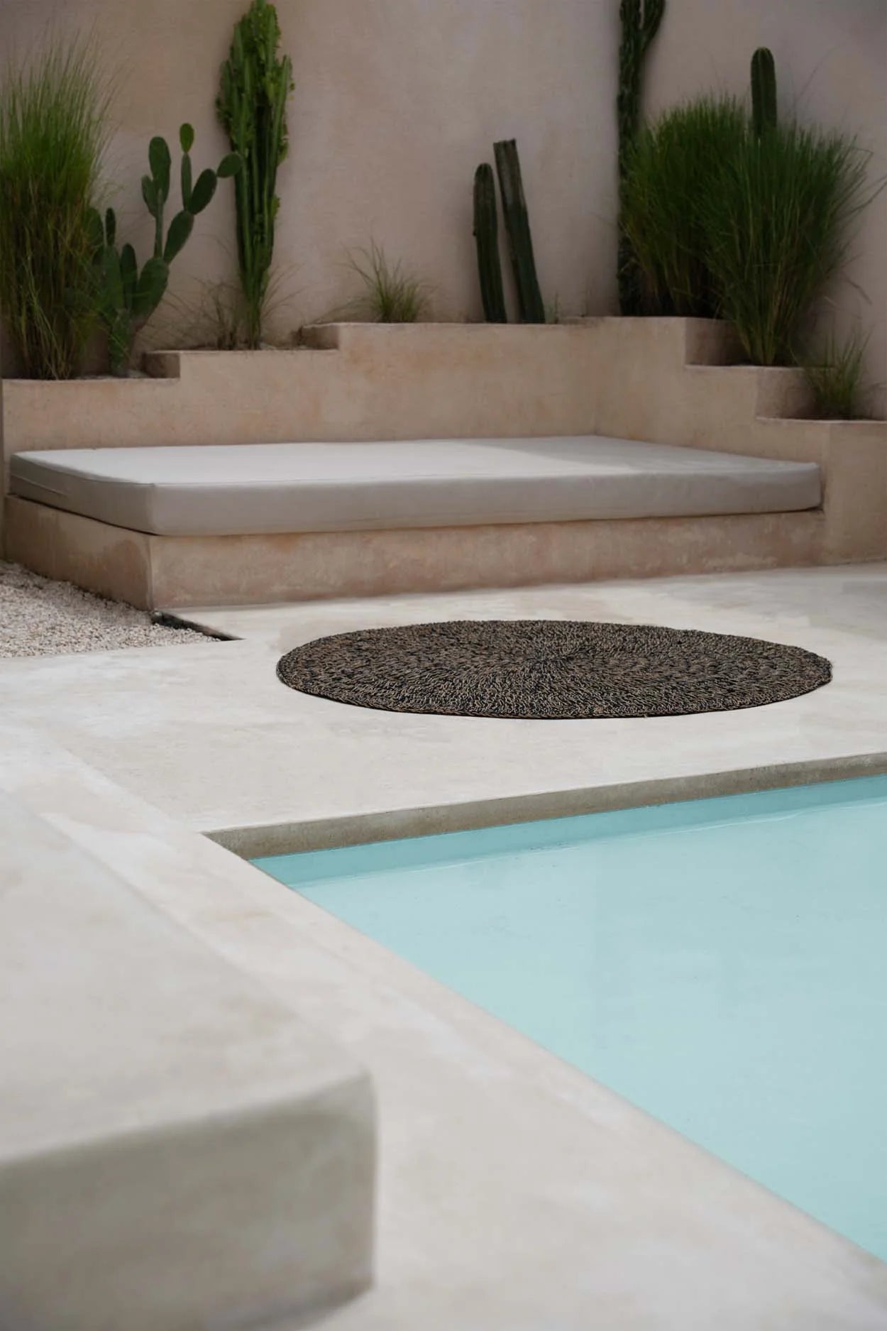 Tapis rond en jonc de mer noir 150 cm dans un espace lounge extérieur avec piscine