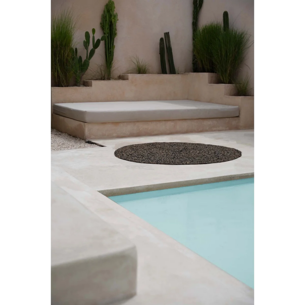 Espace détente extérieur avec banquette, fontaine rocheuse et piscine, Tapis rond en jonc de mer noir 150 cm