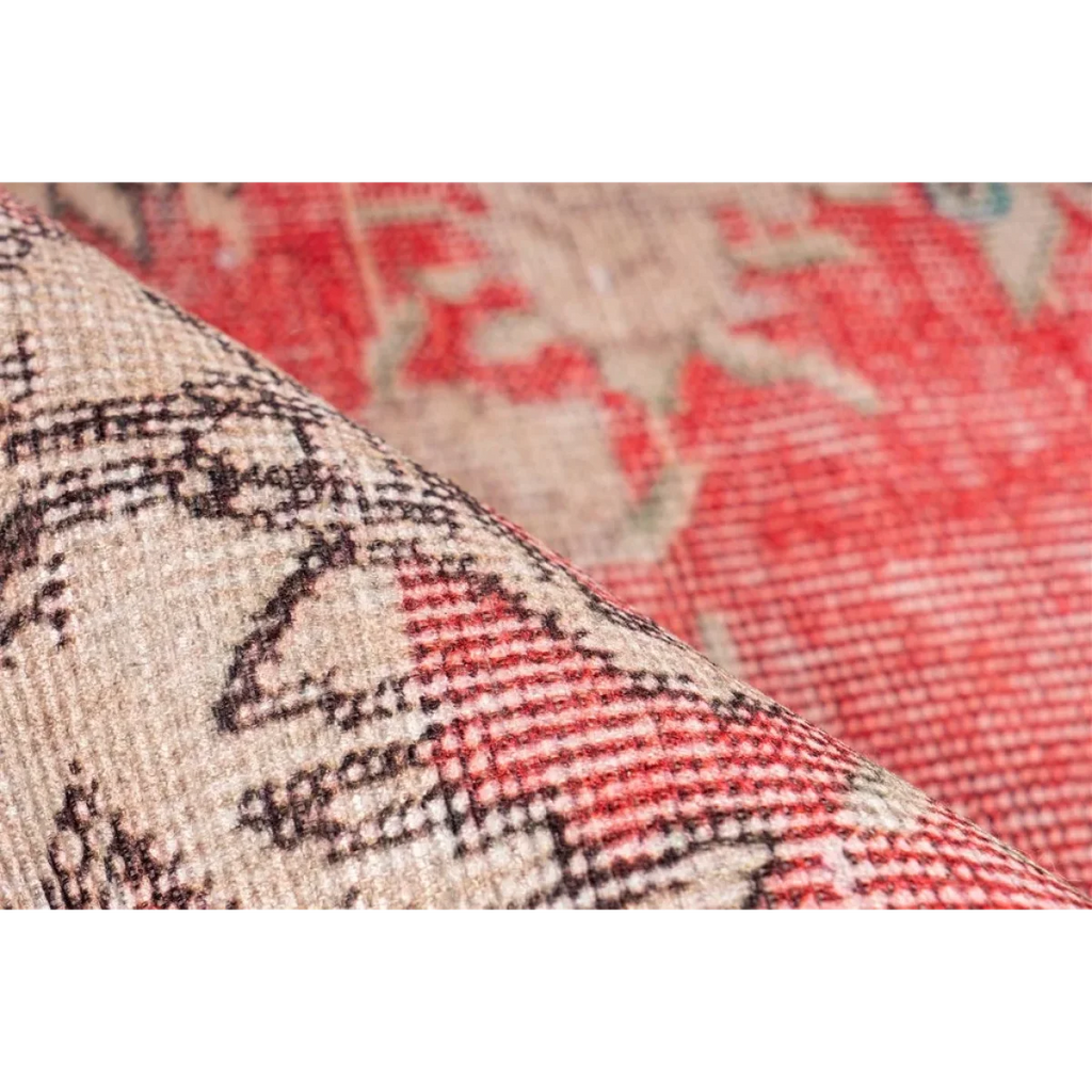 Tapis vintage rouge et beige à motifs, partiellement roulé pour révéler le dessous