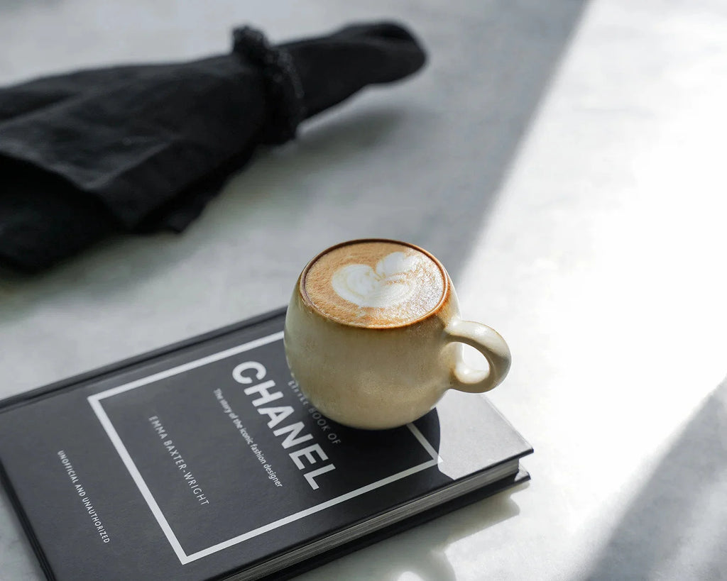 Tasse à espresso en céramique beige avec latte art en forme de cœur sur livre Chanel noir