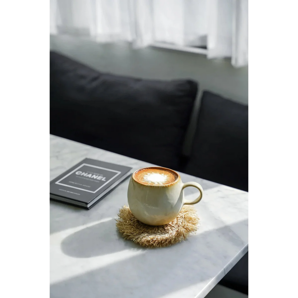 Tasses en céramique arrondies beiges avec latte art sur un dessous de tasse en rotin