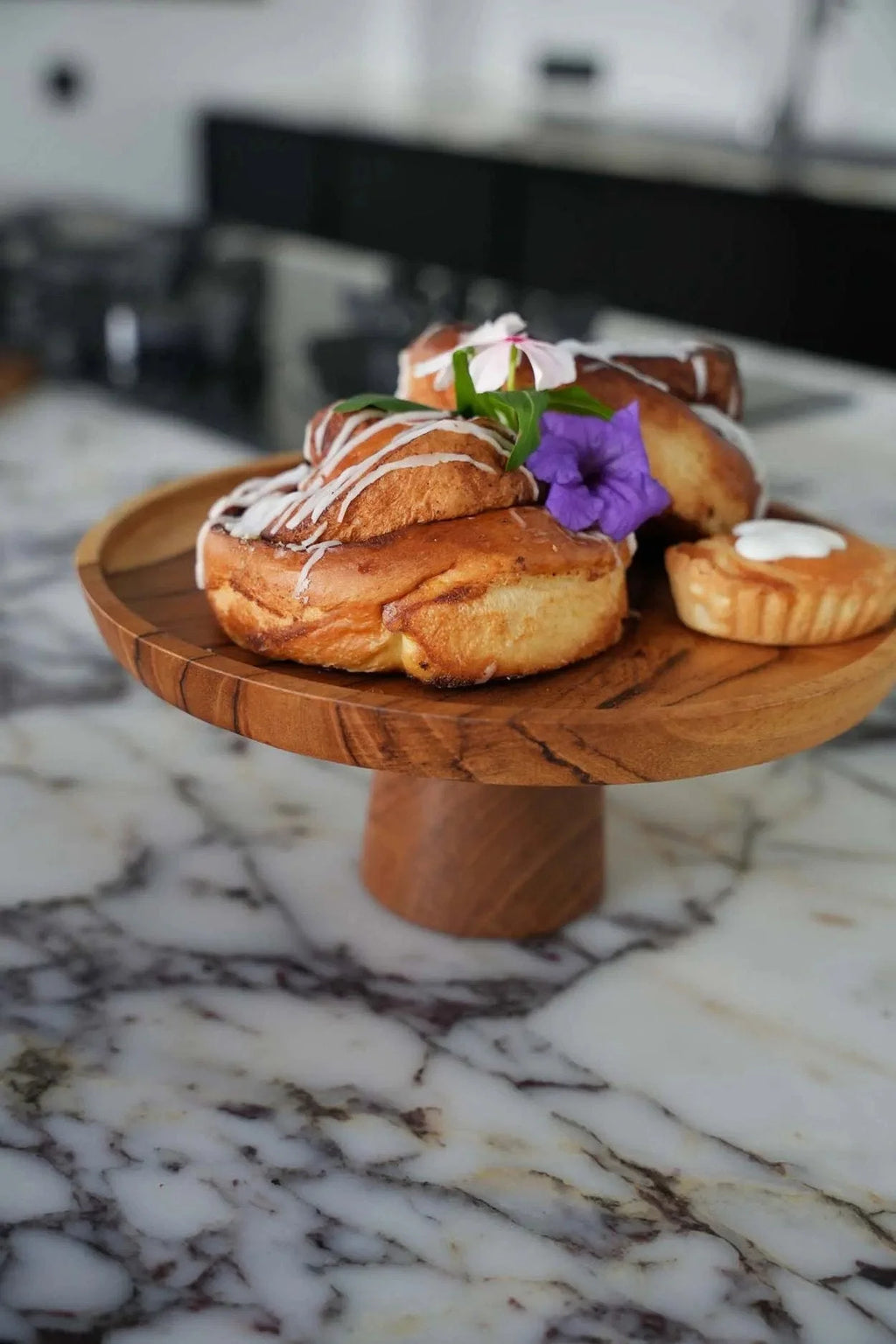 Plateau en teck avec roulés à la cannelle, tarte, fleur violette et feuille verte