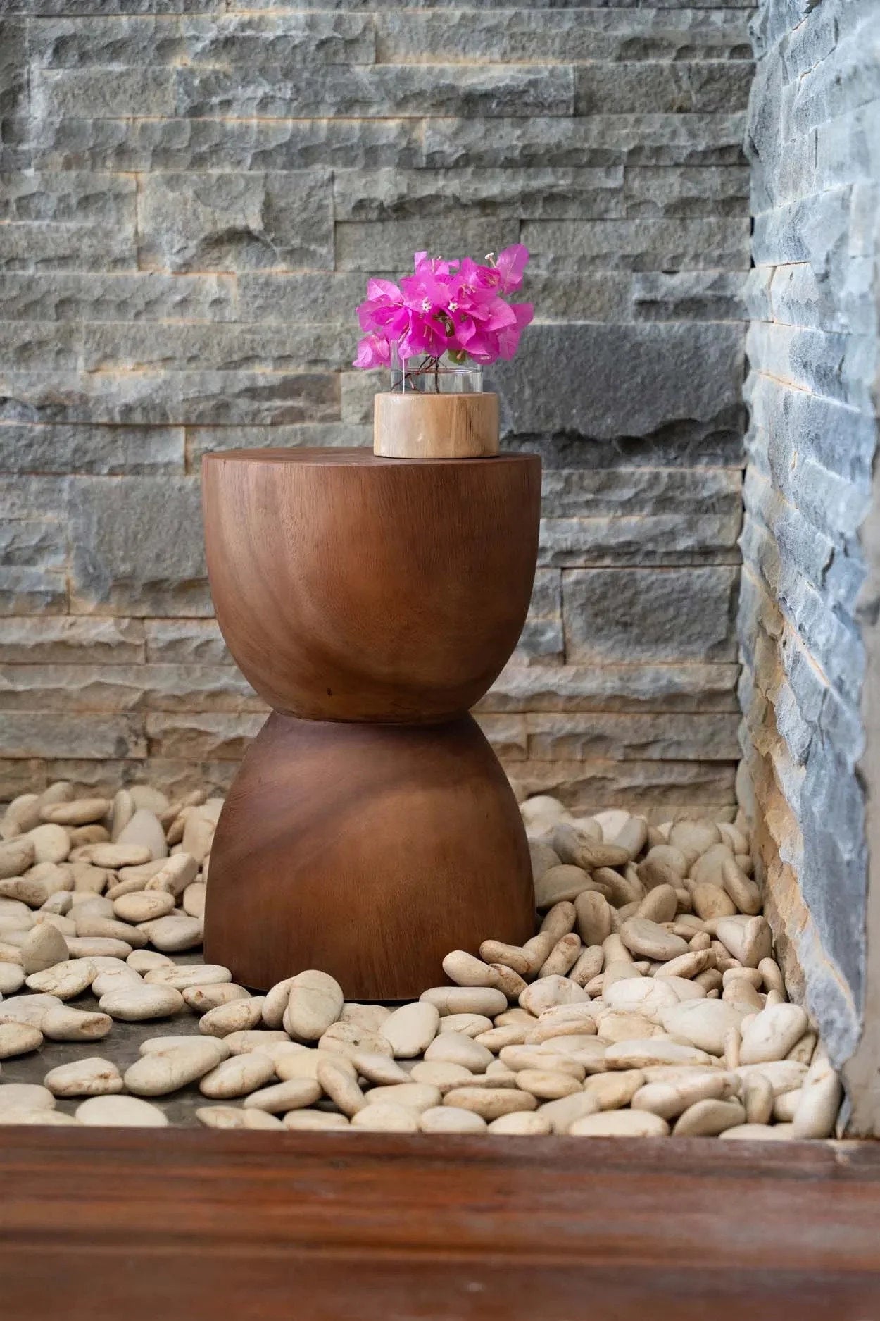 Tabouret en bois brun foncé en forme de sablier avec bouquet de fleurs roses dans un vase en bois clair