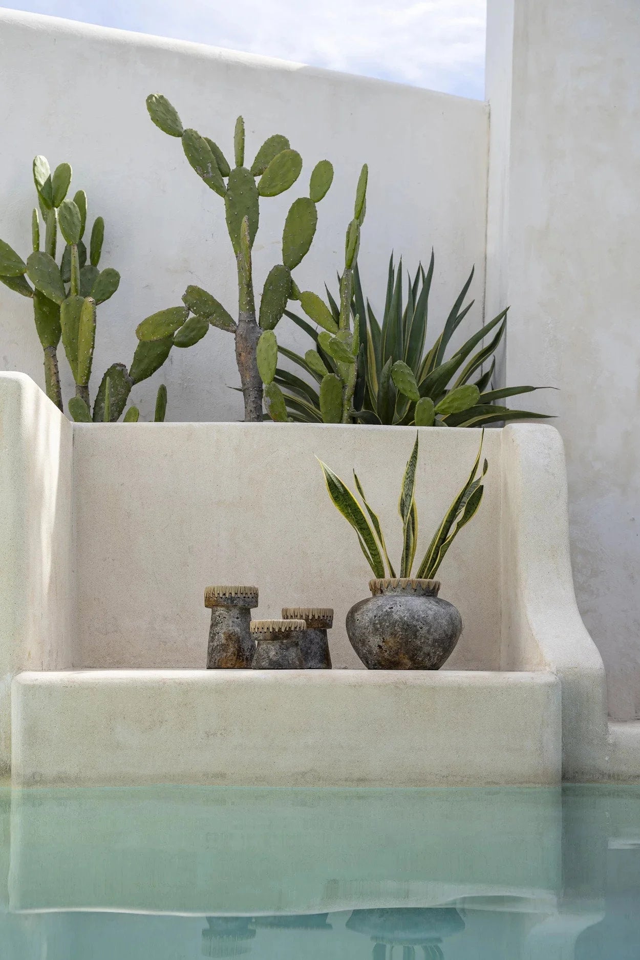 Vase décoratif en terracotta grisée avec raphia tressé et plantes près de la piscine