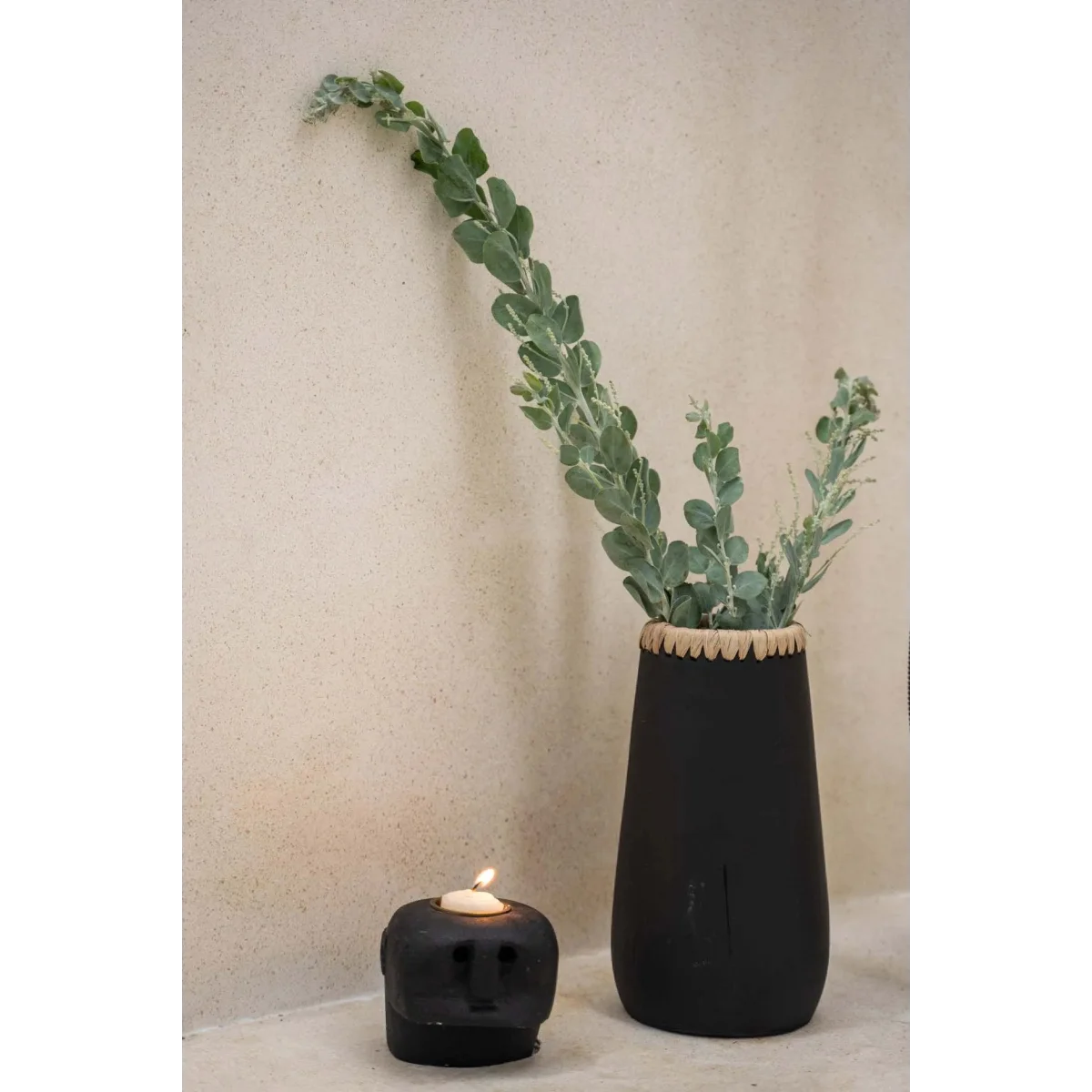 Vase décoratif en terre cuite noire avec raphia, contenant des feuillages verts et blancs