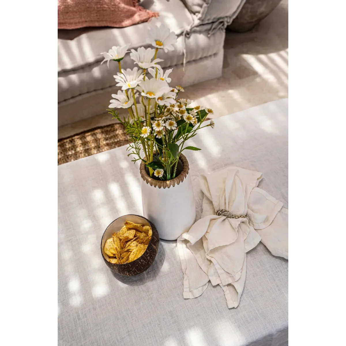 Bouquet de marguerites blanches et jaunes dans un vase en terracotta naturel avec raphia