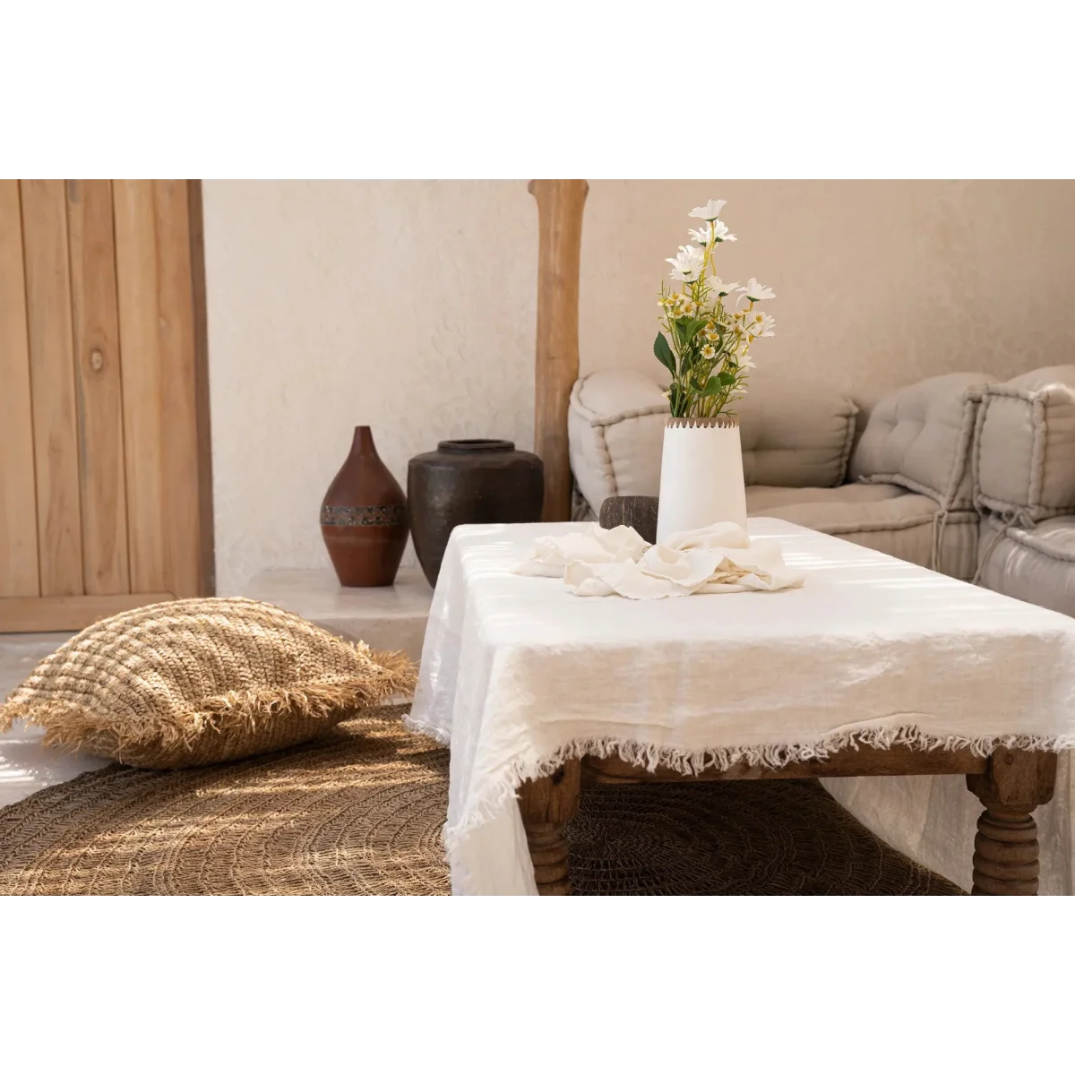 Table en lin clair avec bords effilochés, idéale pour le vase en terre cuite blanc