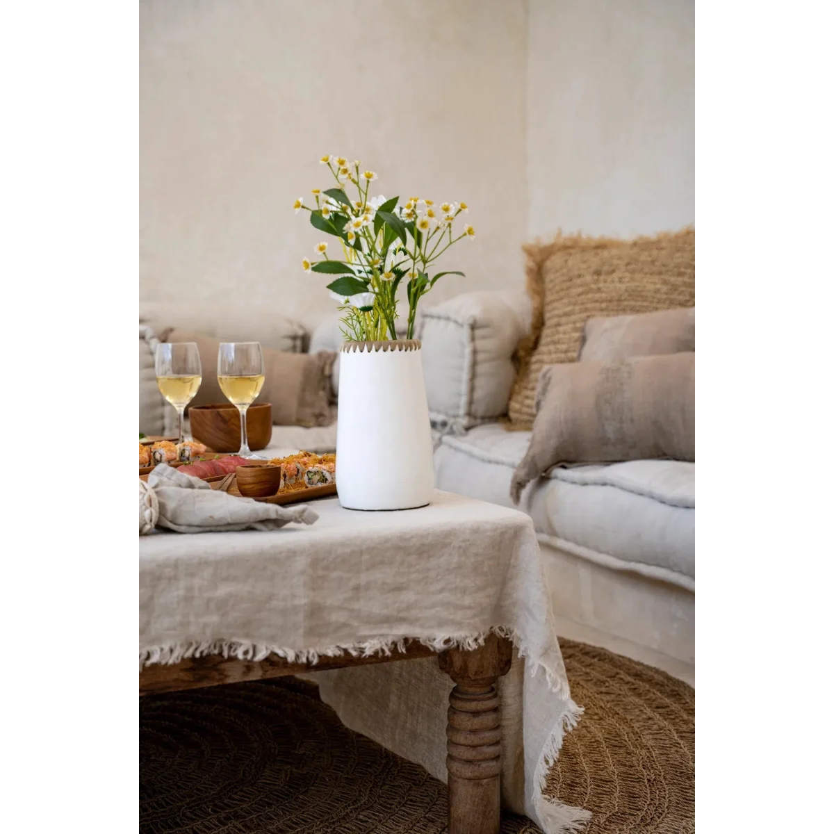 Vase en terre cuite blanc avec bord tressé en raphia rempli de fleurs blanches et jaunes