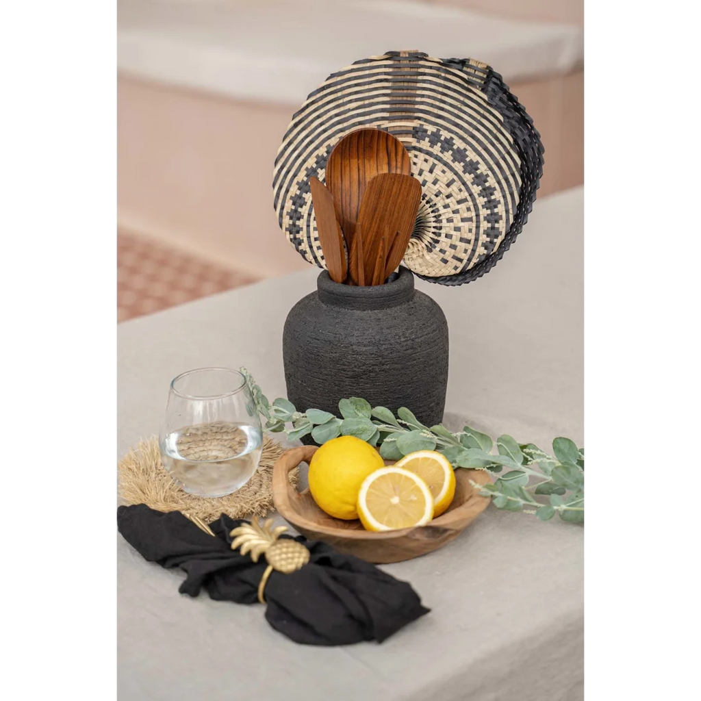 Vase en terre cuite noir à texture côtelée tenant des ustensiles en bois et un trivet tissé