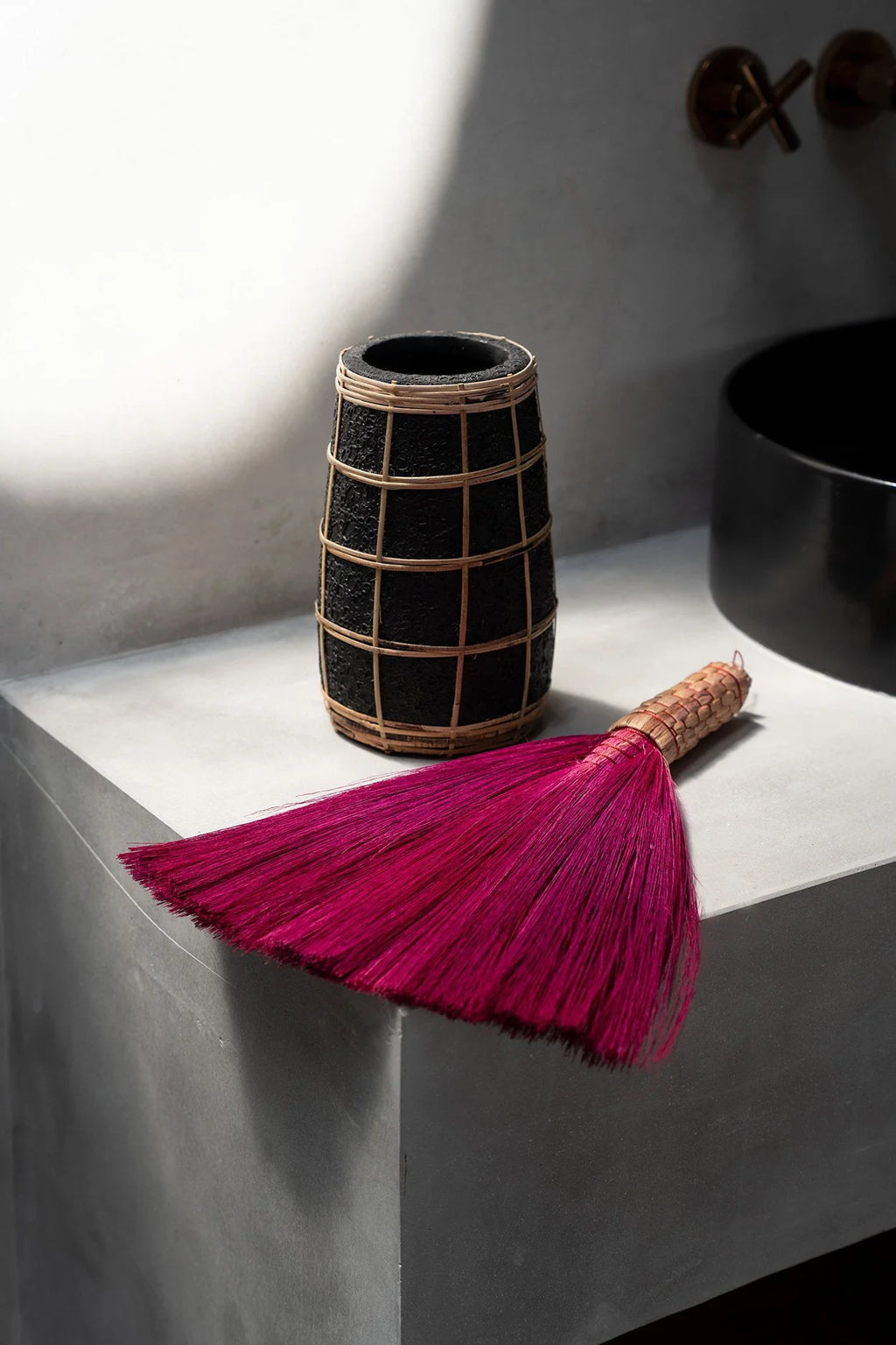 Vase en terre cuite noir avec détail en rotin tressé et un balai-poussière rose