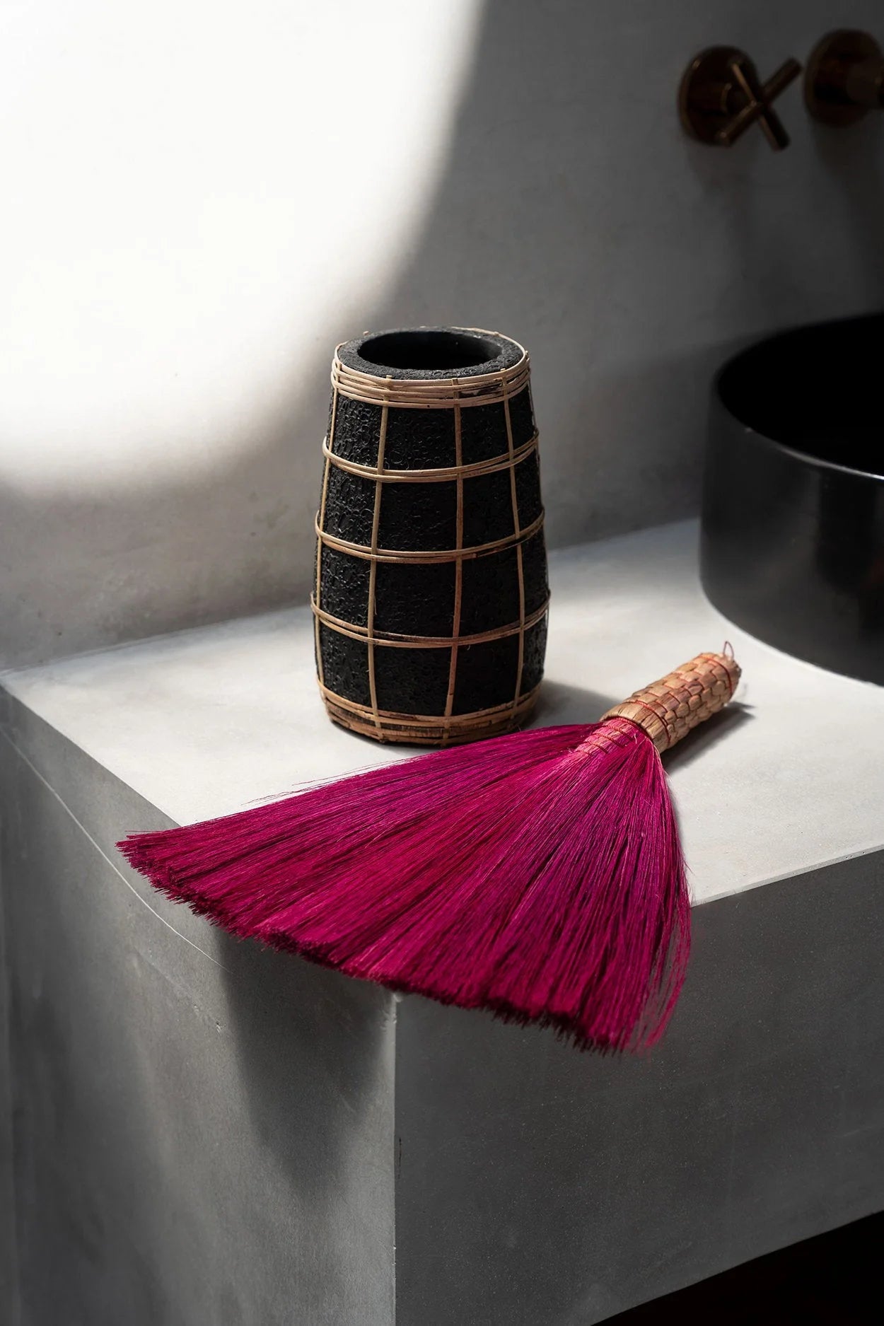 Vase en terre cuite noir avec détail en rotin tressé et un balai-poussière rose