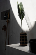 Palme verte dans un vase en terre cuite noir avec détail en rotin tressé
