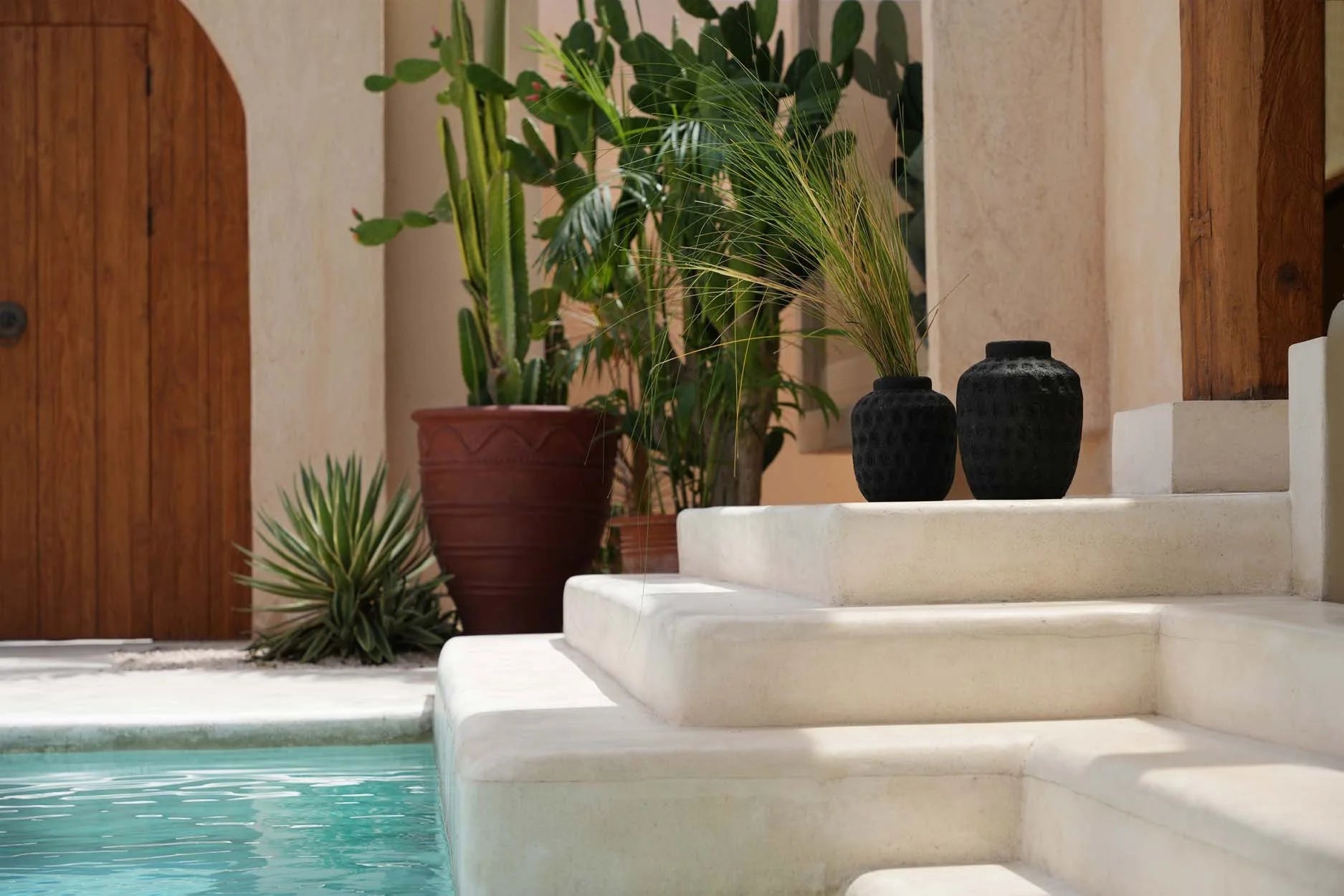 Vase en terre cuite noire arrondie et texturée dans un espace extérieur avec piscine