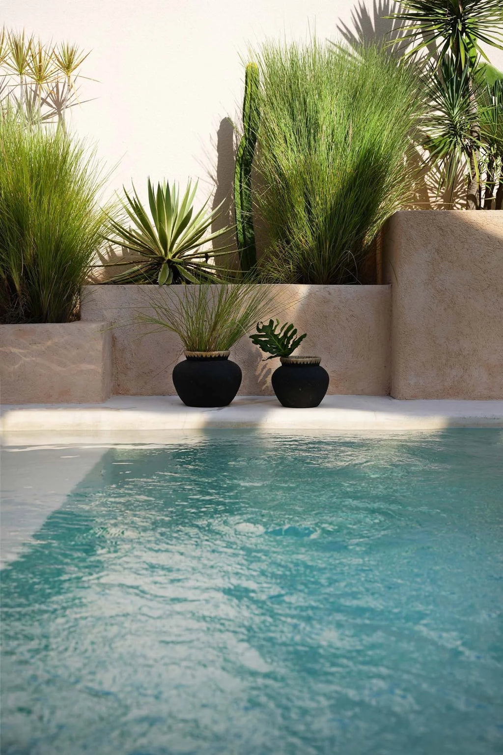 Vase en terre cuite et raphia noir naturel H19 cm devant une piscine turquoise avec plantes en pot
