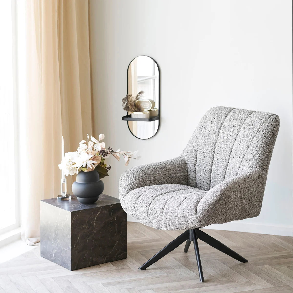 Fauteuil pivotant en tissu gris clair à pois, associé au vase en verre soufflé noir mat