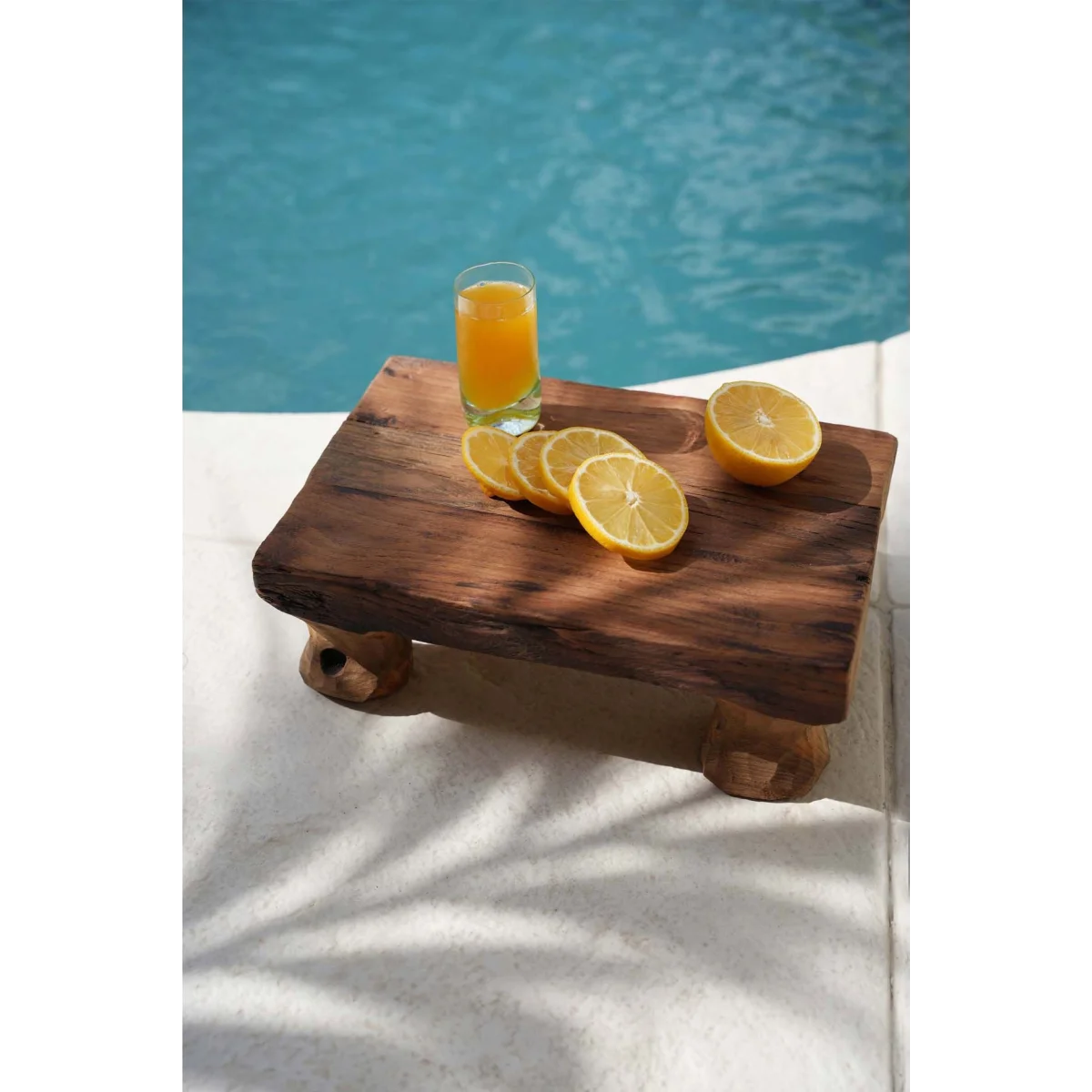 Plateau en bois avec tranches de citron et verre de jus d’orange en bord de piscine